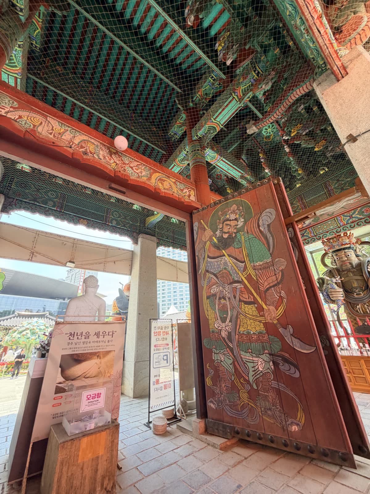 從奉恩寺山門望向江南高樓，門神彩繪與都市天際線同框