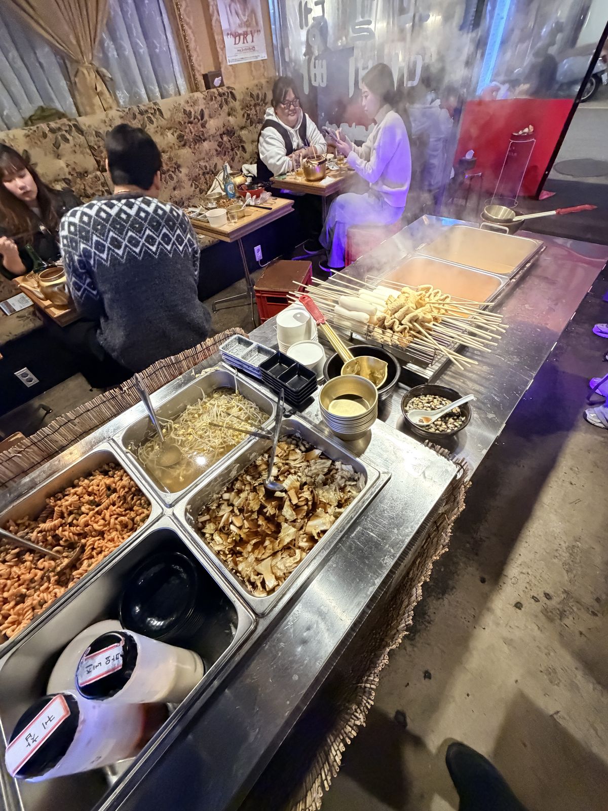 自助吧不鏽鋼檯面,擺著涼拌通心粉、豆芽、醃漬蔬菜與魚板串
