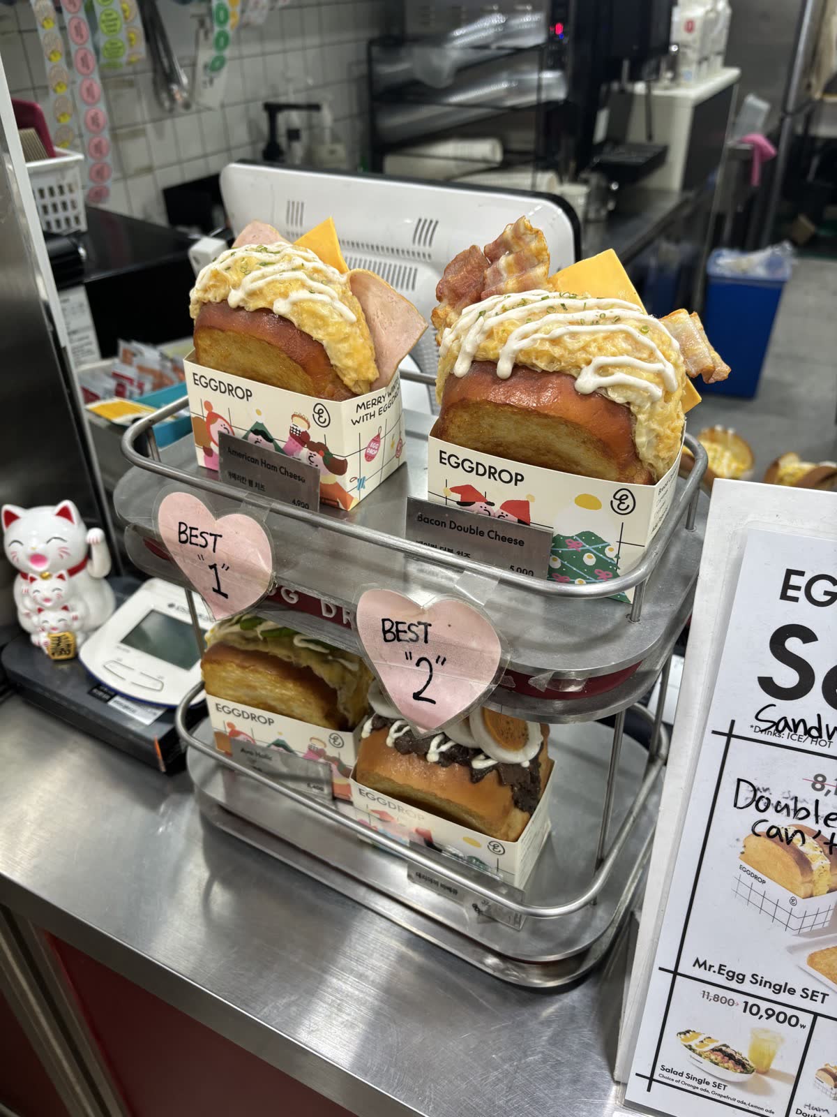 櫃檯展示的 Egg Drop 食物模型，標示 American Ham Cheese、Bacon Double Cheese 等人氣款