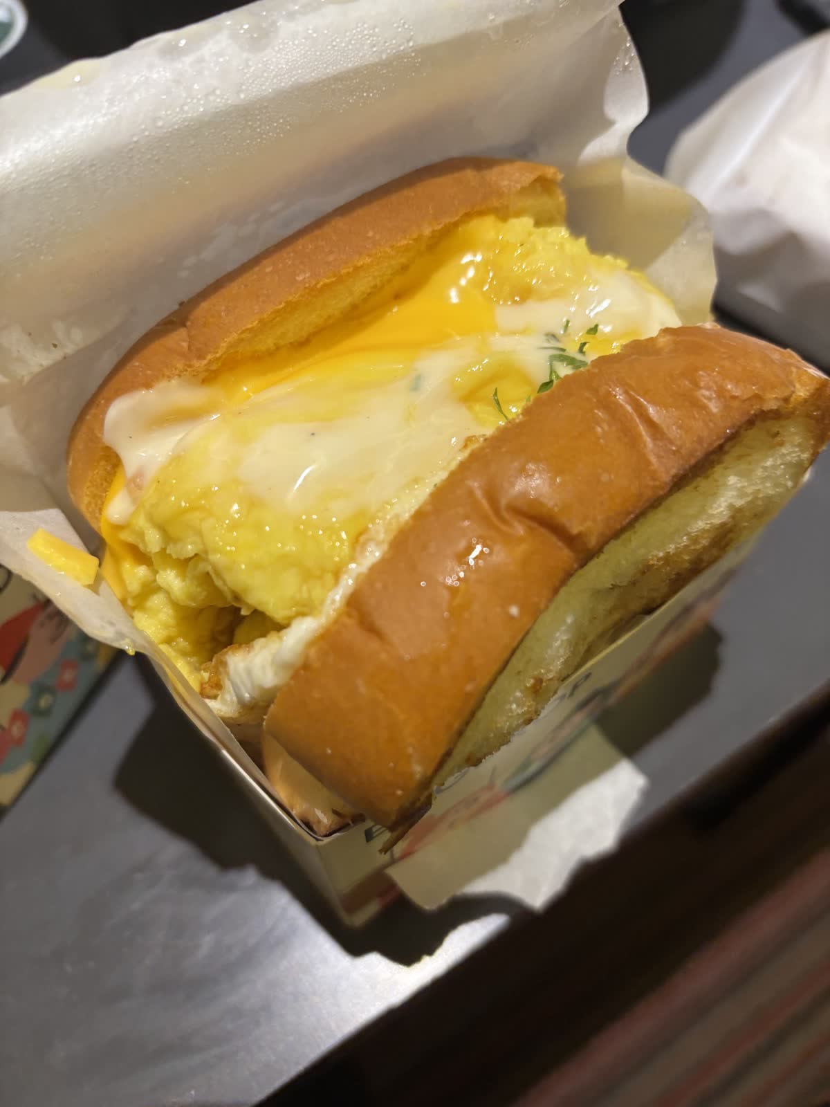 Egg Drop 厚片吐司夾滿滑嫩炒蛋與起司，淋上白色醬汁的特寫