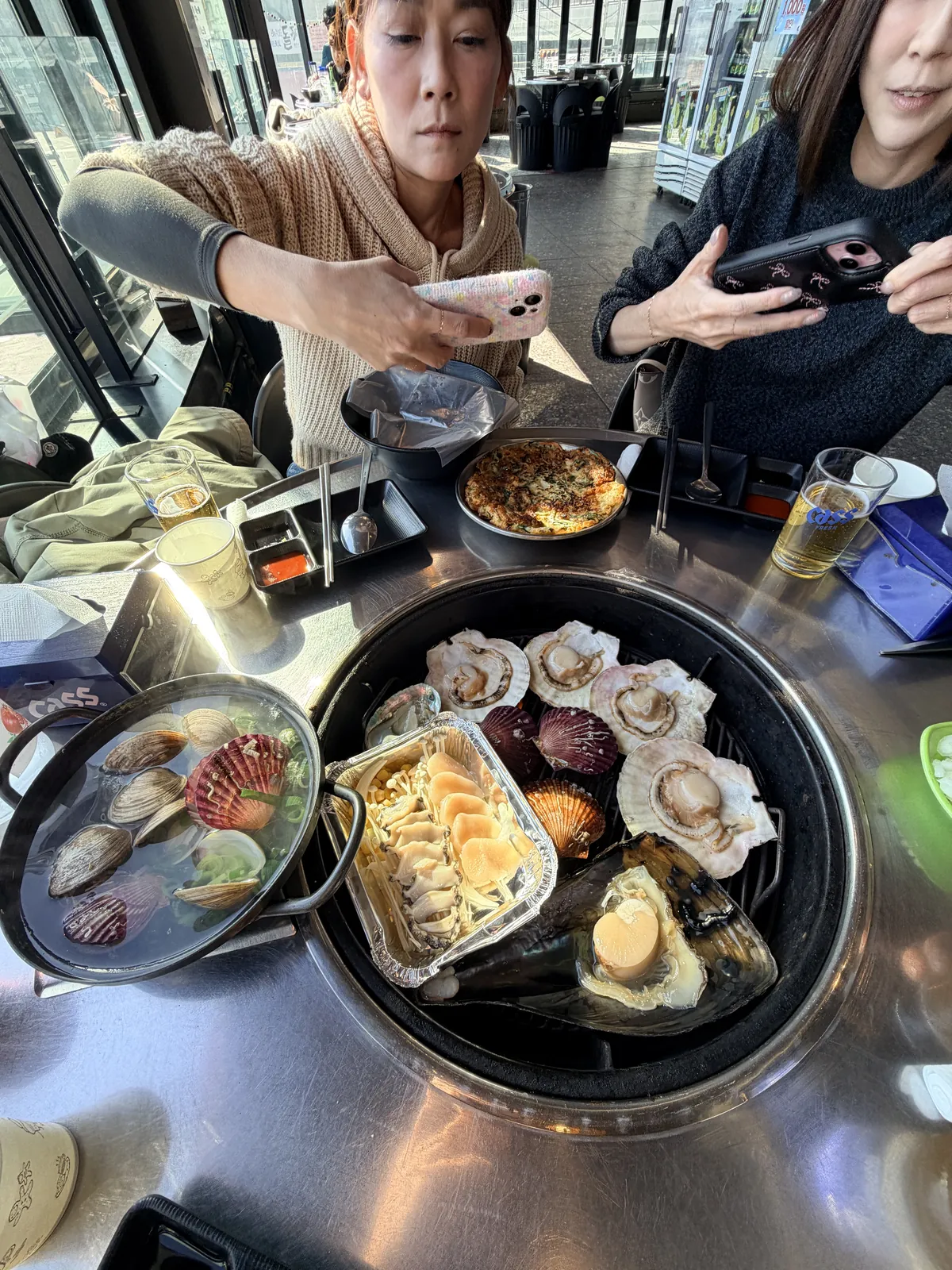 圓形烤盤上同時加熱多種貝類與鋁箔盒海鮮，旁邊備有起司