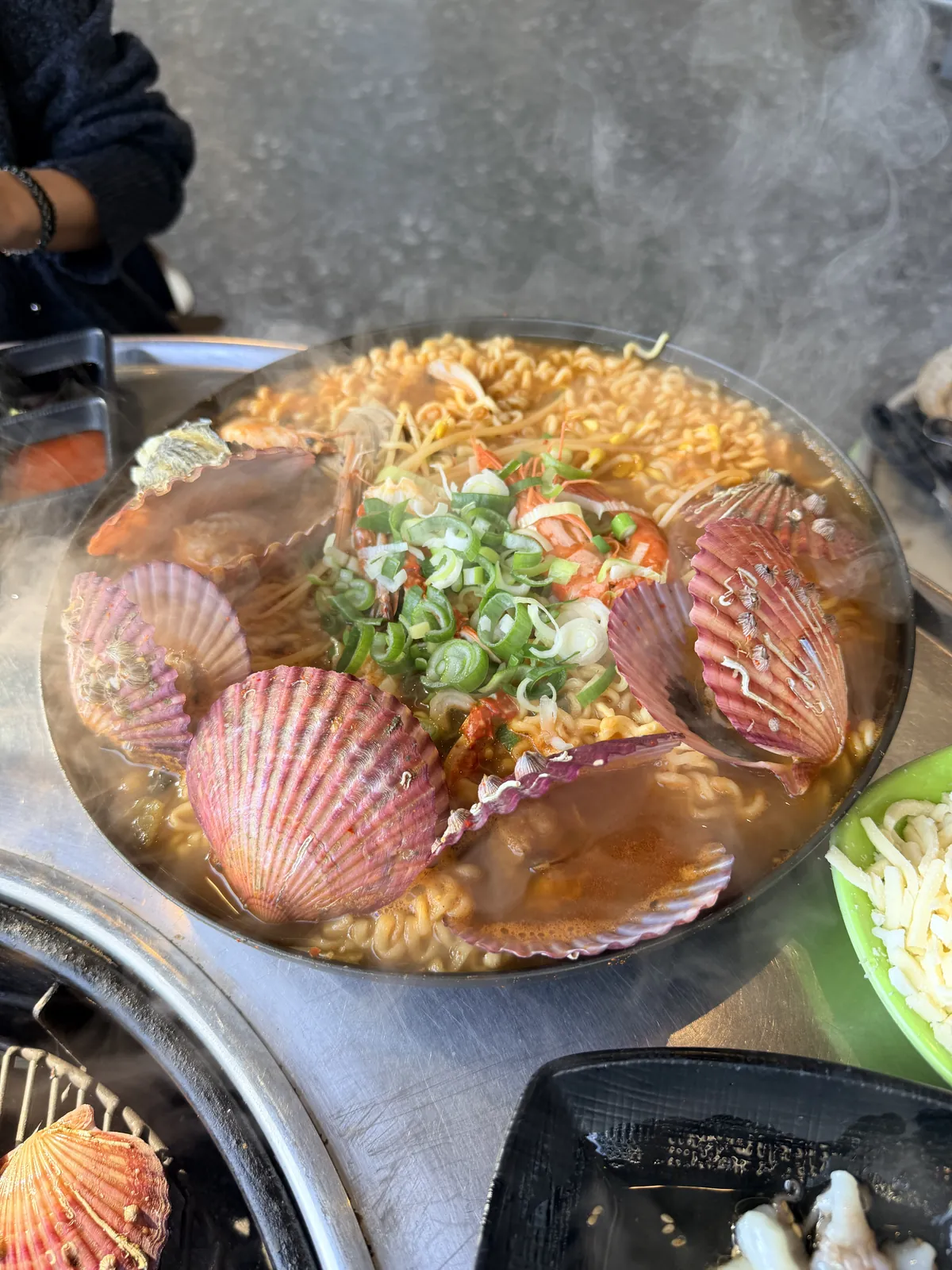 熱氣上升的海鮮拉麵，鍋中有扇貝、蝦、豆芽與蔥花