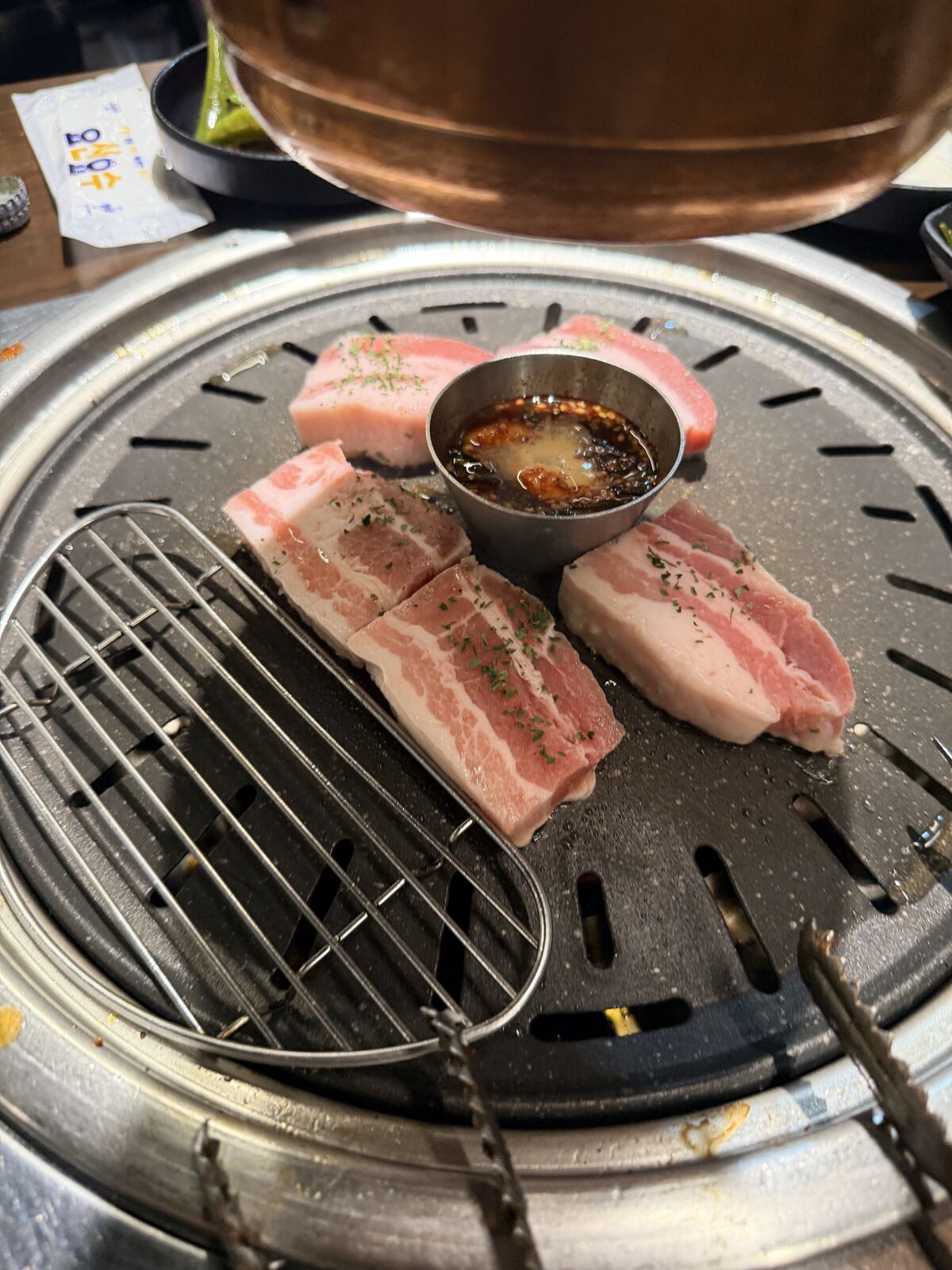 烤盤上肥瘦相間的厚切五花肉與中央金屬醬碗